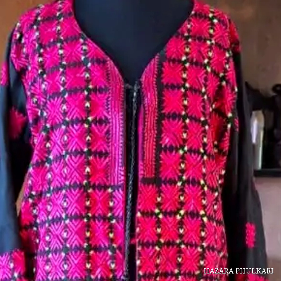 Close detail of a Phulkari coat showing dense counted-thread embroidery in magenta, red and black across the front panels