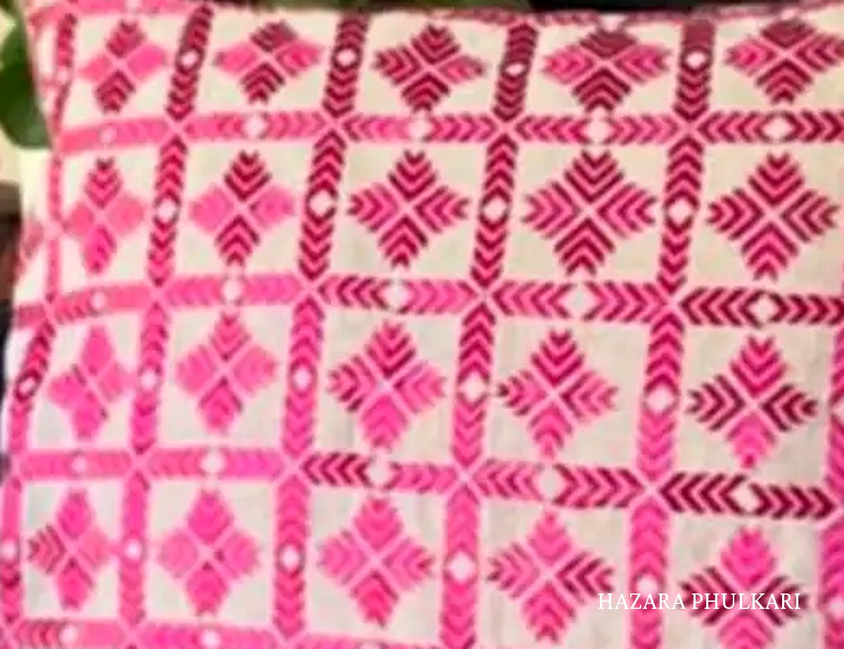 Close detail of a Phulkari cushion cover showing counted-thread pink embroidery forming a grid of diamond motifs