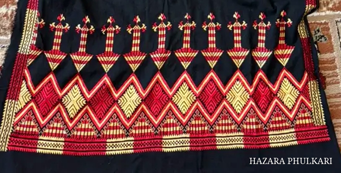 Close detail of a Phulkari stole border showing red and golden counted-thread embroidery in a zig-zag and diamond pattern on black fabric