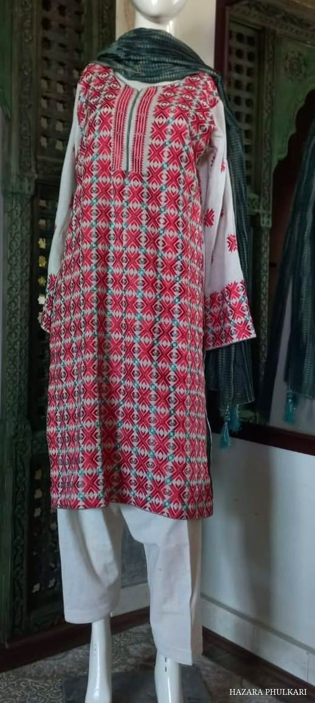 Handmade Phulkari shirt in ivory fabric embroidered with dense red and turquoise geometric motifs, styled with a green dupatta on a mannequin